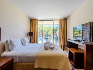 Une chambre d’hôtel avec un lit, une télévision, un bureau et une vue sur une piscine et des palmiers.