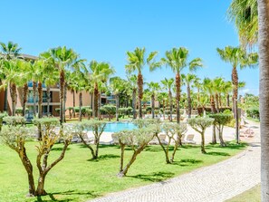 Un complexe hôtelier doté d’une piscine, de palmiers et d’une promenade dallée.