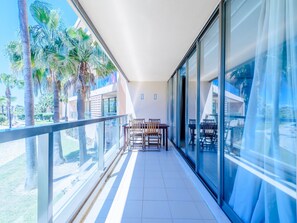 A balcony with a glass railing, a table with chairs, and palm trees in the background. - Apartment  by Interhome (Guia)