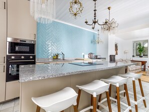 A modern kitchen with a large island, bar stools, a microwave, and a chandelier. - Apartment  by Interhome (Tavira)