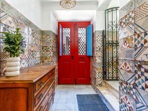 A hallway with a red door, patterned tiles, a wooden cabinet, and a potted plant. - Apartment  by Interhome (Tavira)