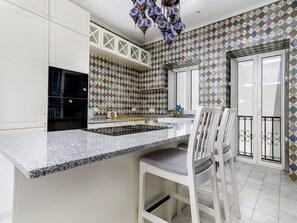Une cuisine dotée d’un plan de travail en granit, de meubles blancs et d’un dosseret carrelé à motifs.
