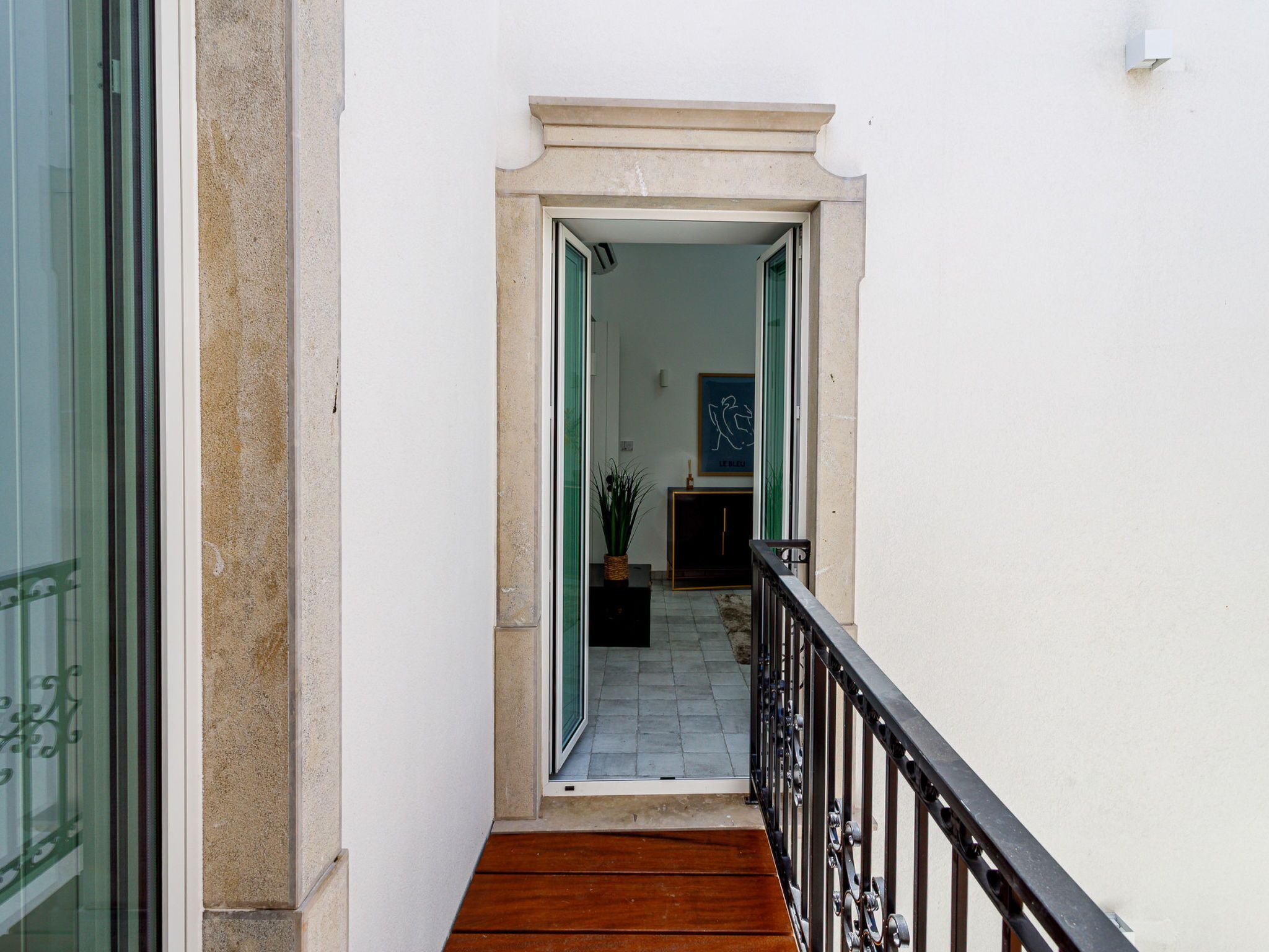 Una escalera estrecha que lleva a un cuarto con una puerta verde, una planta en maceta y un cuadro en la pared.