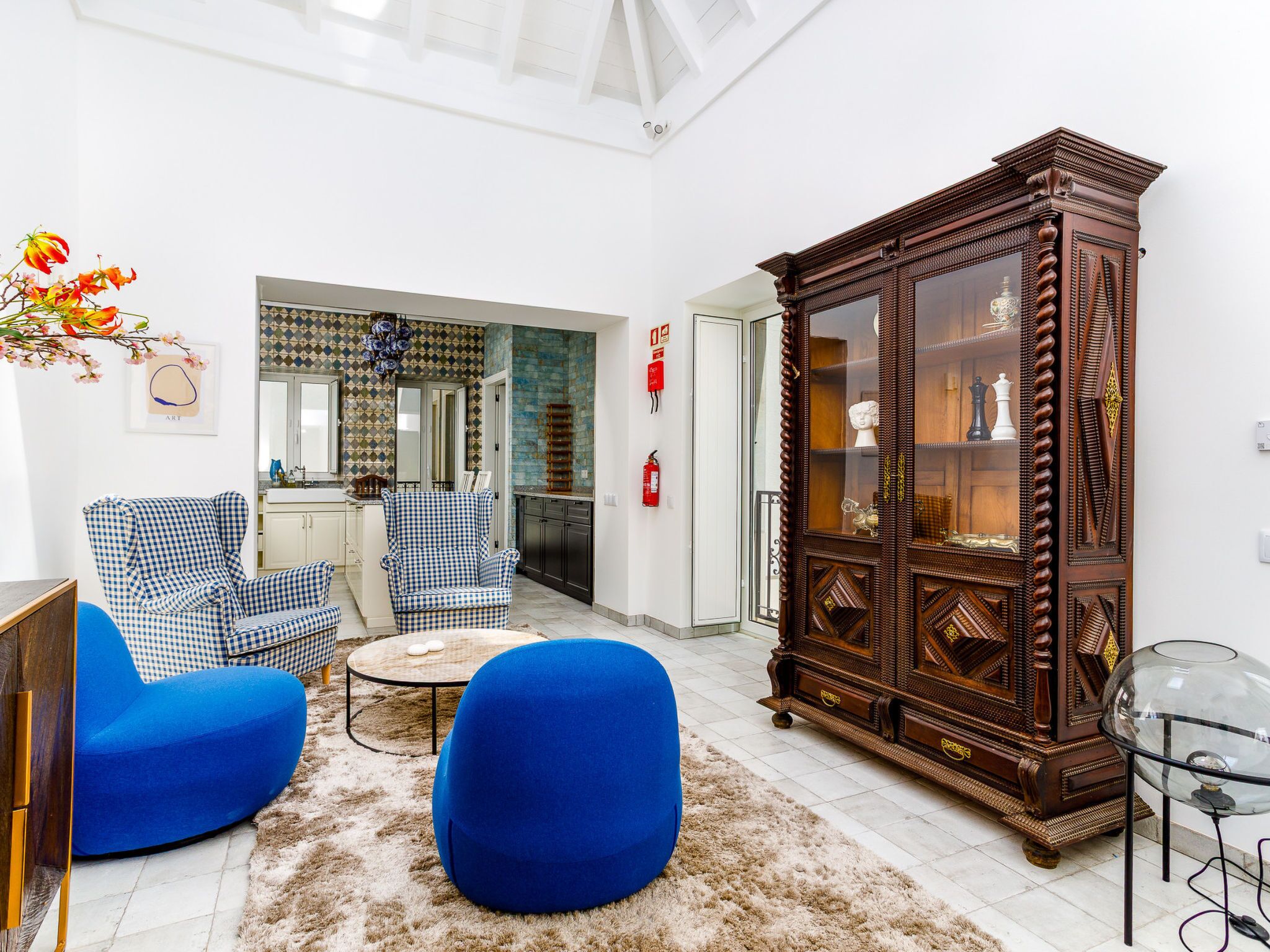 Un salon avec des fauteuils bleus, une table basse, un meuble en bois et, au fond, une cuisine.