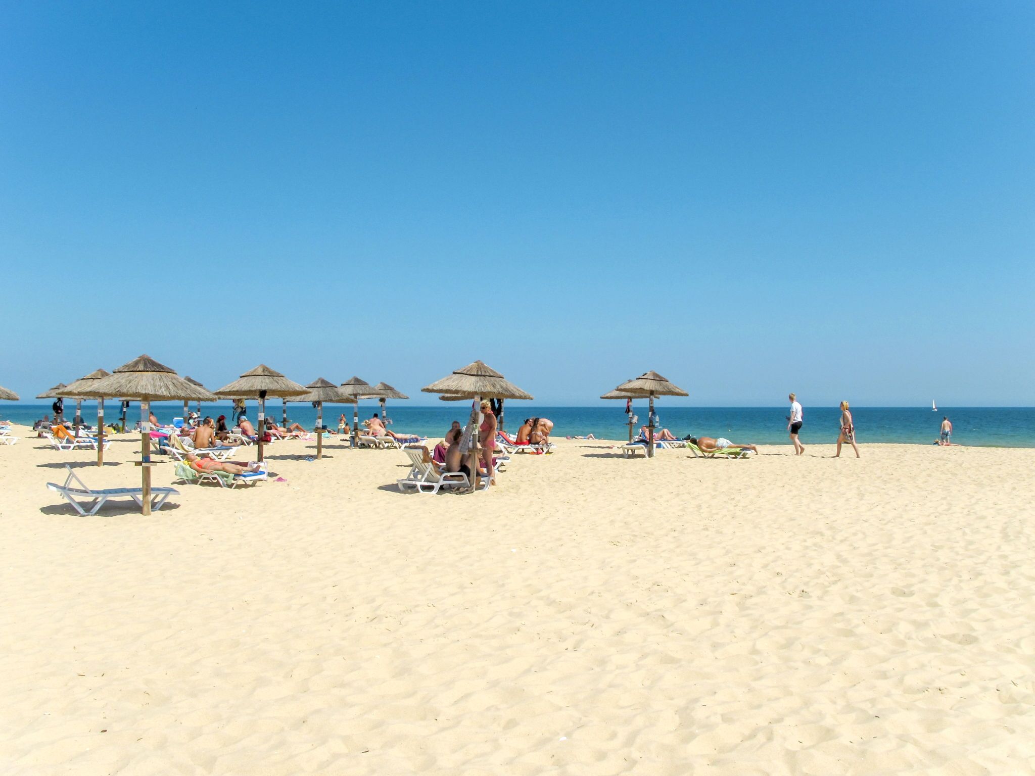 Een strand met ligbedden en rieten parasols.