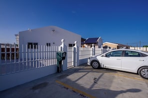 A parking area with a white car, a gated entrance, and a building with a blue roof. - Aruba Vibe Apartments #2 | A charming place near the beaches and the city center (Oranjestad)