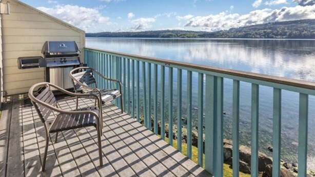 Eine Terrasse mit Grill und Stühlen mit Blick auf einen stillen See.