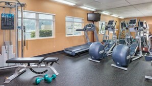 Ein Fitnessraum mit Trainingsgeräten, einer Bank, Kurzhanteln und einem Fernseher an der Wand.