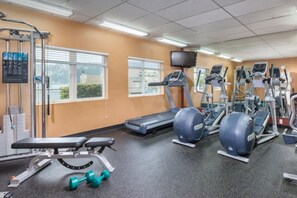 A gym with exercise equipment, a bench, dumbbells, and a television on the wall. - WM BLOCK Discovery Bay 2br (Port Townsend)