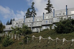 A multi-story building with balconies, surrounded by trees and a stone wall. - WM BLOCK Discovery Bay 2br (Port Townsend)