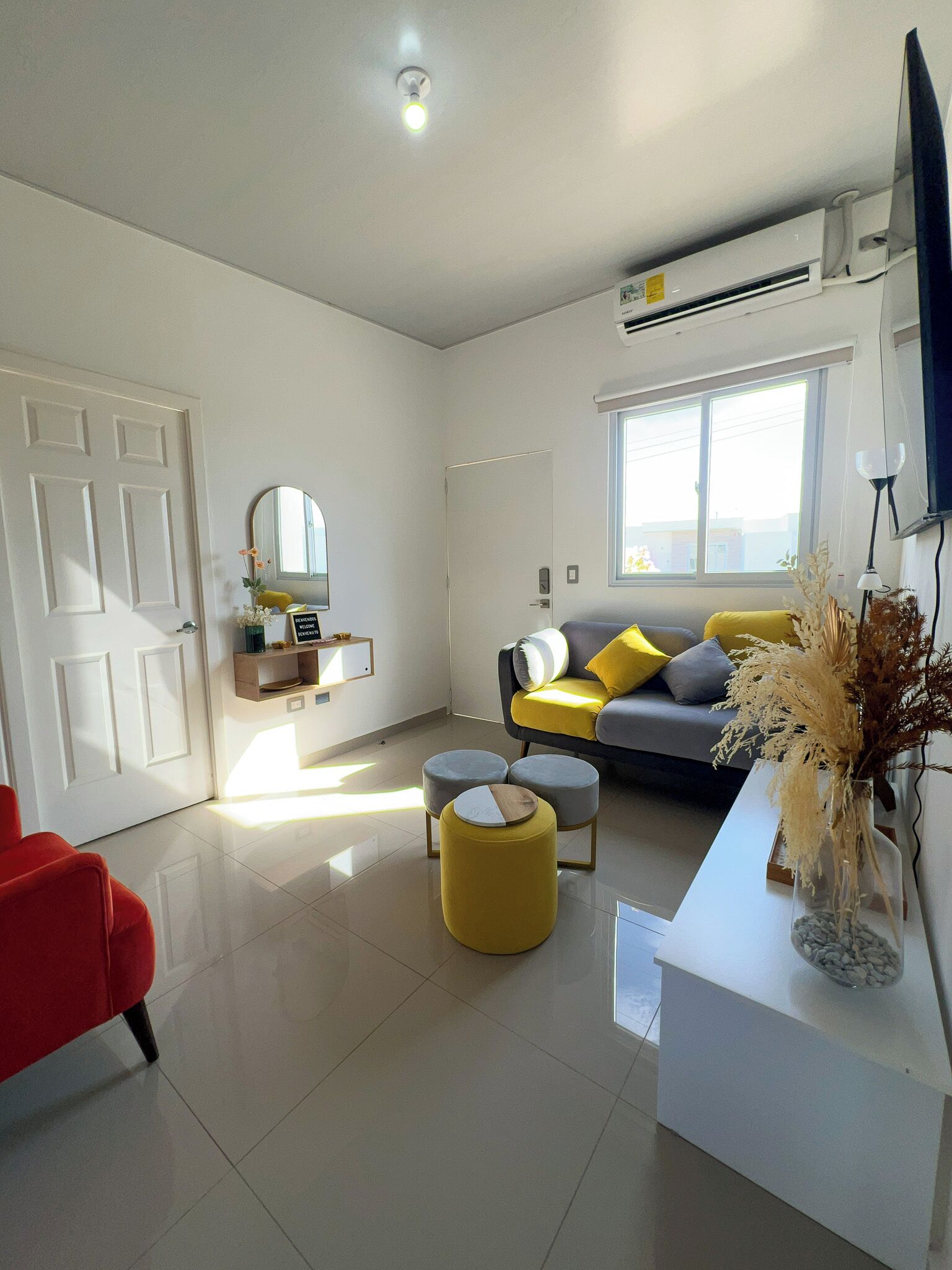 A modern living room with a sofa, ottomans, a red chair, a white console table, and a mirror.