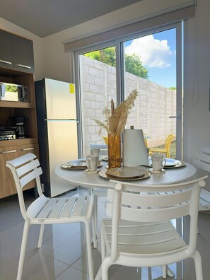 A modern kitchen with a dining area, featuring a large window, white chairs, and a table set for two. - Home in San Miguel (San Miguel)