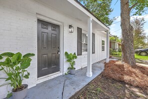 A white house with a dark front door, two potted plants, and a tree with pine needles on the right. - That 70s house retro style! Great outdoor space. (Goose Creek)