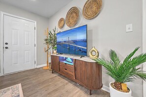 Een woonkamer met een televisie op een houten kast, een deur en een potplant.