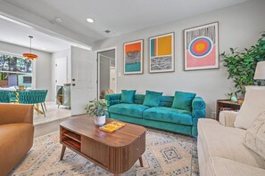 Een moderne woonkamer met een blauwgroene bank, een houten salontafel en een kamerkleed met een patroon.