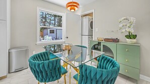Eine moderne Küche mit einem Glastisch, blaugrünen Stühlen, einer Waschmaschine und einem grünen Schrank mit Dekorationselementen.