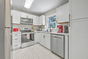 A modern kitchen with white cabinets, a microwave, a toaster, a coffee machine, and a dishwasher. - That 70s house retro style! Great outdoor space. (Goose Creek)