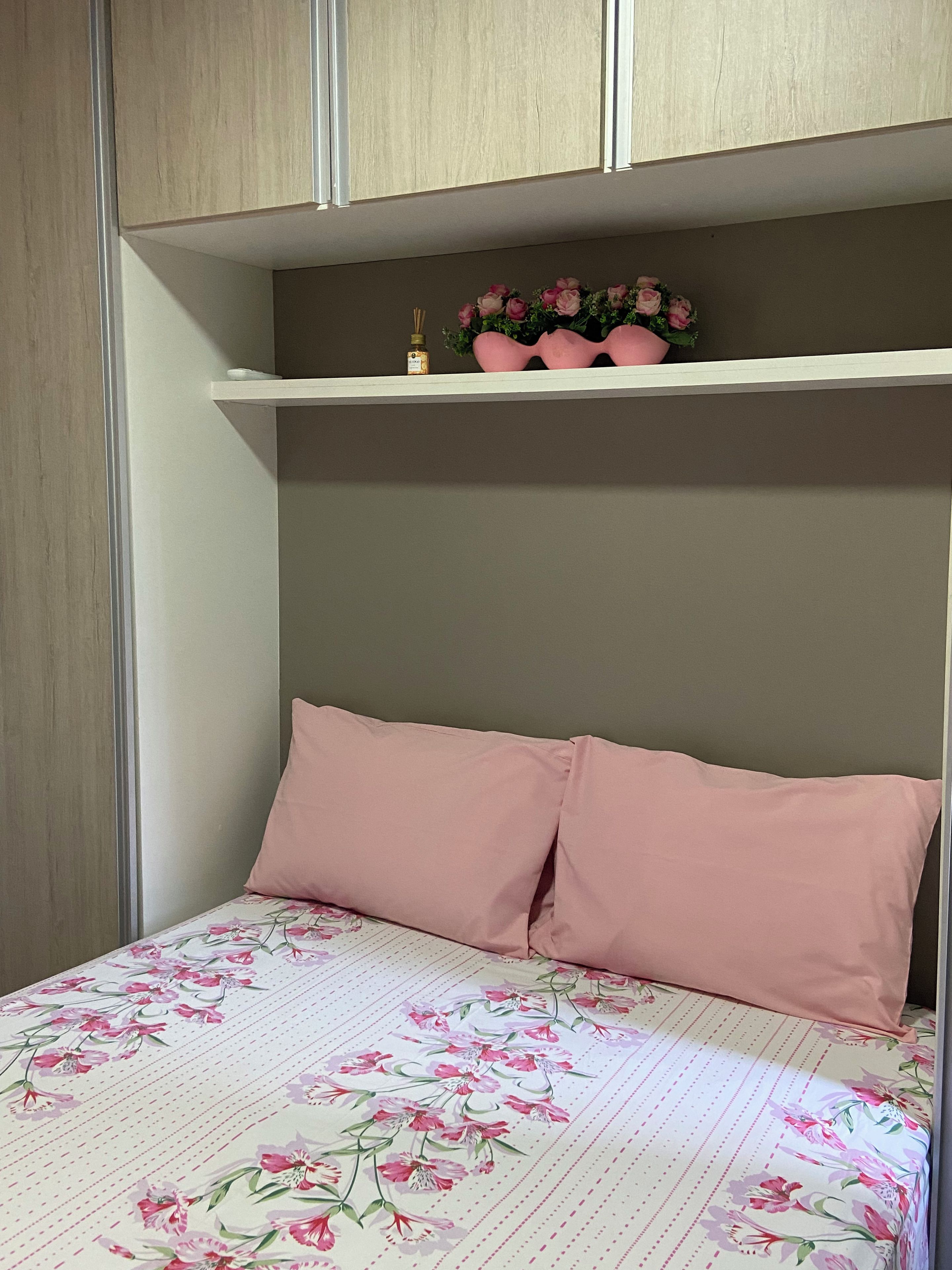 Un dormitorio con cama, dos almohadas, repisas con adornos y una colcha estampada con motivos florales.