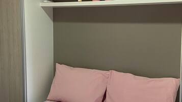 Un dormitorio con cama, dos almohadas, repisas con adornos y una colcha estampada con motivos florales.