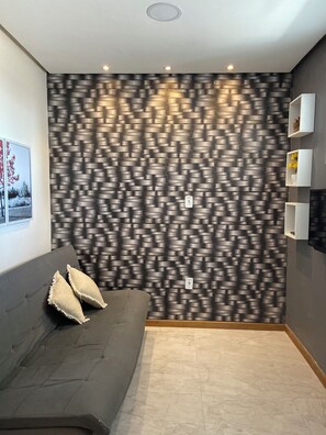 Una habitación moderna con pared texturizada, un sofá gris con cojines y un pequeño mueble blanco.