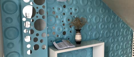 A reception area with a blue textured wall, a white console table, a vase with dried flowers, and a hanging light fixture.