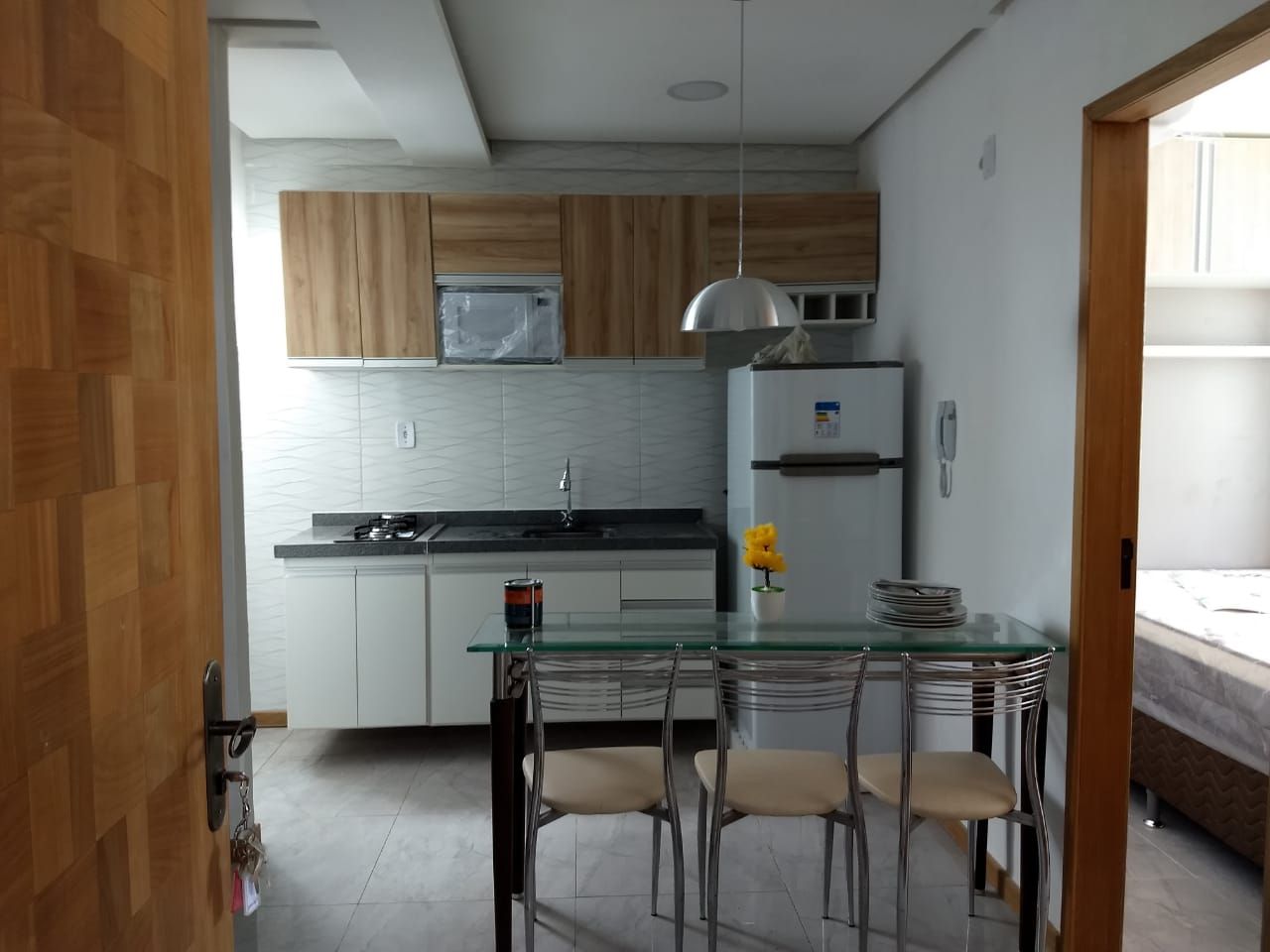 Una cocina compacta con una mesa de comedor de vidrio, armarios de madera y un refrigerador.