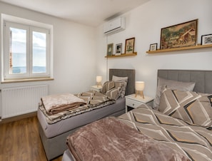 Ein Schlafzimmer mit zwei Betten, einem Fenster, einer Klimaanlage und einem Bild an der Wand.