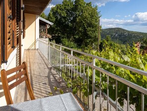 Ein Balkon mit einem Holzbalken, einem Stuhl und einem Tisch, mit Blick auf einen Weinberg und eine gebirgige Landschaft.