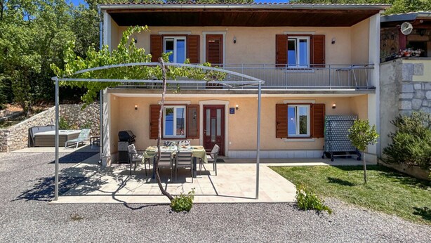 Ein zweistöckiges Gebäude mit einem Balkon, einer Sitzgelegenheit im Freien und einem kleinen Garten.