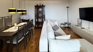 Ein modernes Wohnzimmer mit Essbereich, einer Sofagarnitur, einem Schrank und einem Flachbildfernseher.