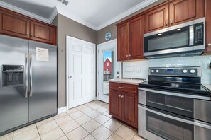A kitchen with stainless steel appliances, wooden cabinets, and a tiled floor. - "Pipe Dreams" -- 50 Steps To Beach, Gulf View, Dog Friendly, Super Cute 3BR Home (Gulf Shores)