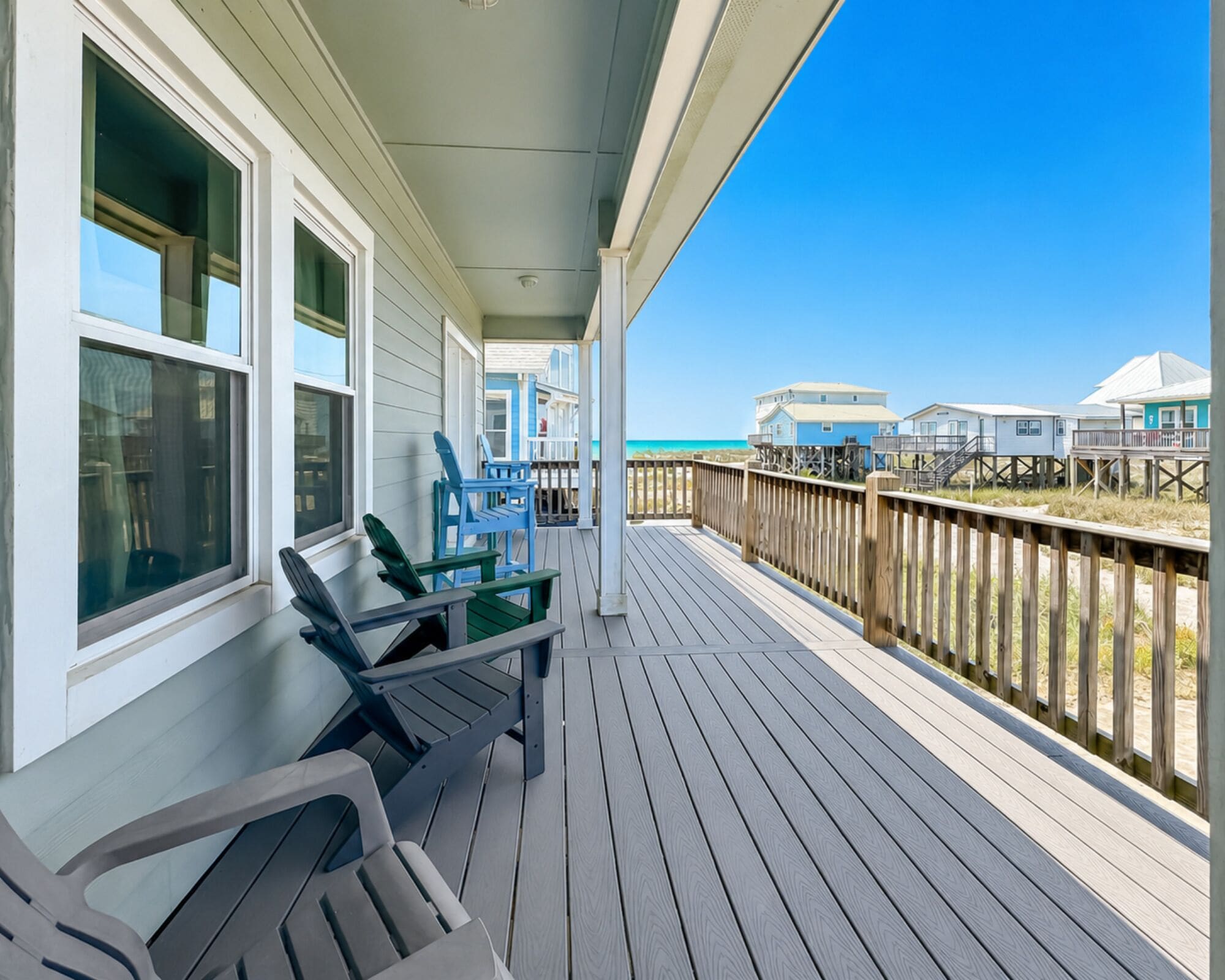 A wooden deck with outdoor furniture, overlooking a beach with beach houses.