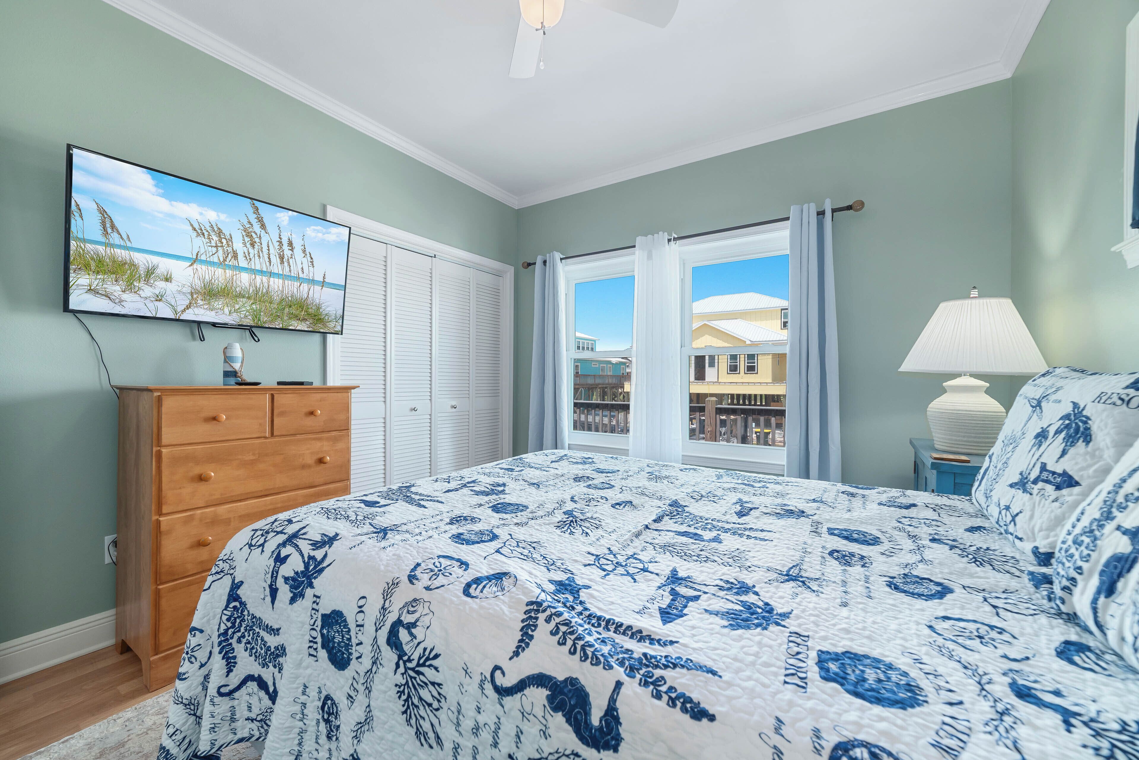 Un dormitorio con cama, cómoda, televisor y ventana con cortinas.