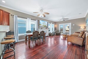 A spacious living area with hardwood flooring, a dining table with chairs, a sofa, and a ceiling fan. - "Pipe Dreams" -- 50 Steps To Beach, Gulf View, Dog Friendly, Super Cute 3BR Home (Gulf Shores)