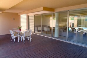 A modern outdoor patio with a wooden deck, a table with chairs, and a glass sliding door leading to an adjacent room. - Villa Salgados private pool (Guia)