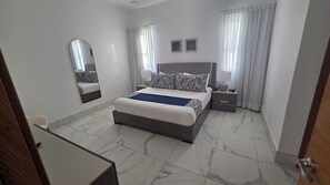Ein Hotelzimmer mit Bett, Nachttisch, Spiegel und einem Fenster mit Vorhängen.