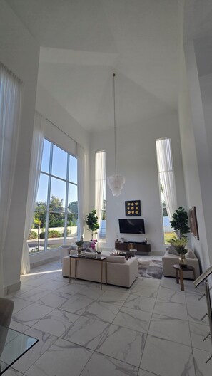 A spacious living room with a large window, a chandelier, a flat-screen TV, and a sofa. - Sophisticated 3 to 7 bedroom Royal Villas @ Lifestyle Holidays, Puerto Plata, DR (Cofresi)