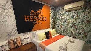 A hotel room with a bed, pillows, a blanket, a wall-mounted air conditioner, and a floral wallpaper.