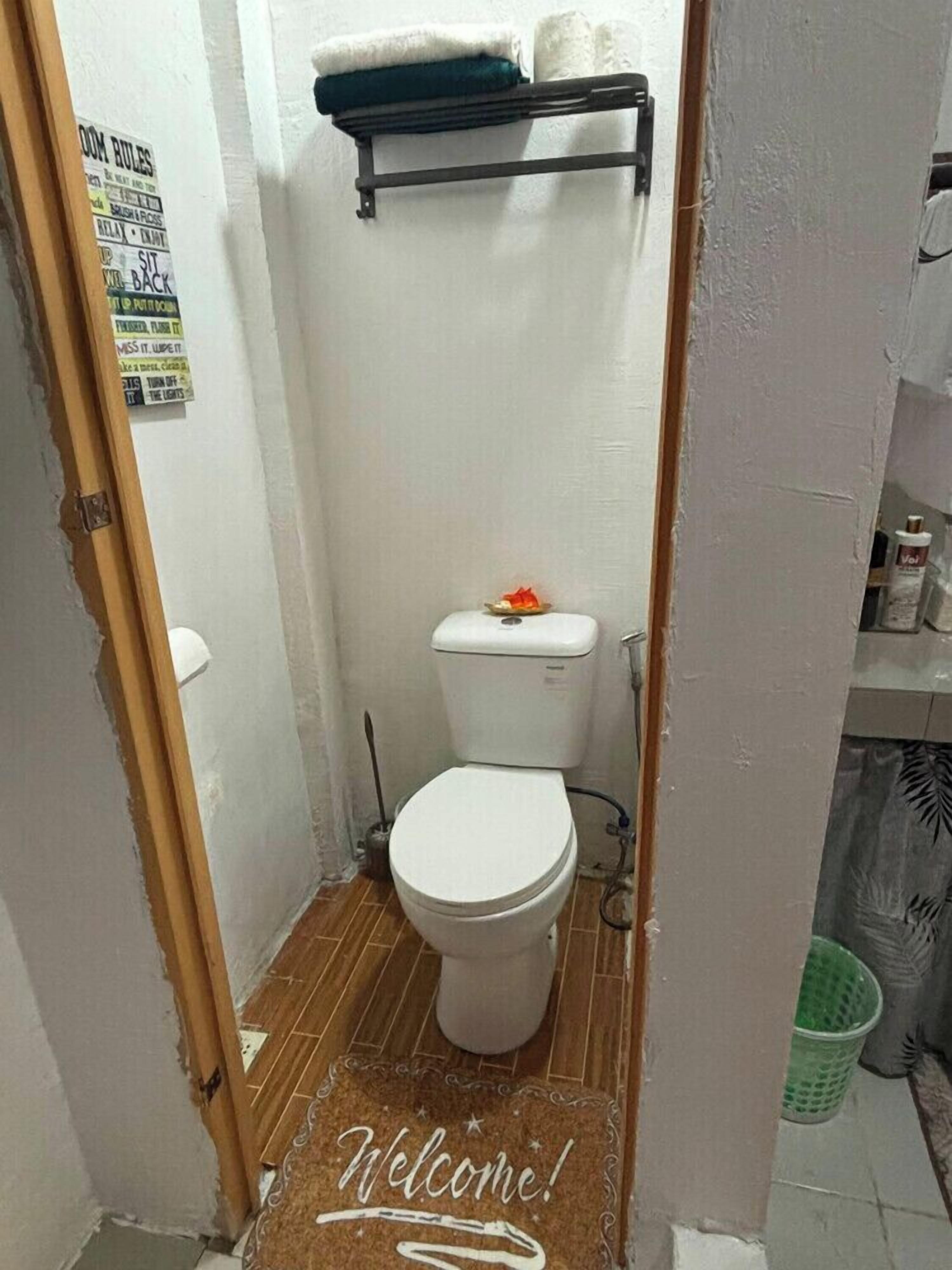 A small bathroom with a toilet, a shower curtain rod, and a welcome mat.