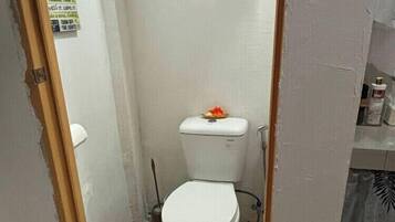 A small bathroom with a toilet, a shower curtain rod, and a welcome mat.