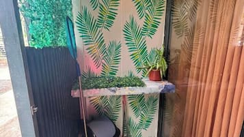 Un espacio reducido con una pared decorada con motivos de hojas verdes, un estante pequeño con una planta en maceta y una escoba apoyada contra la pared.