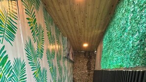 A narrow corridor with a wooden ceiling, walls with a leaf pattern, a small wooden table with items, and a green artificial turf floor.