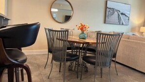 A dining area with a round table, four chairs, a vase with flowers, a round mirror, and a painting on the wall. - Phoenix Orange Beach 1202 (Orange Beach)