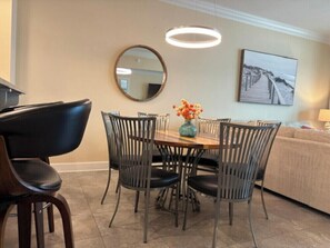 A dining area with a round table, four chairs, a vase with flowers, a round mirror, and a painting on the wall. - Phoenix Orange Beach 1202 (Orange Beach)