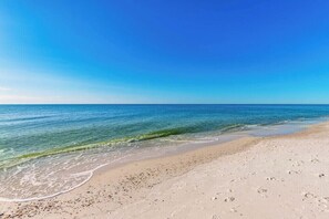A beach with clear blue water, sandy shore, and footprints. - Phoenix Orange Beach 1202 (Orange Beach)