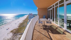 A balcony with a view of a beach and ocean, a table with chairs, and a railing. - Phoenix Orange Beach 1202 (Orange Beach)