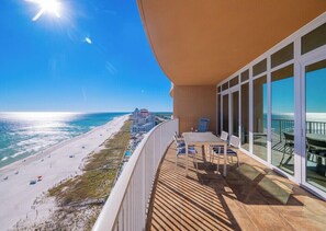 A balcony with a view of a beach and ocean, a table with chairs, and a railing. - Phoenix Orange Beach 1202 (Orange Beach)