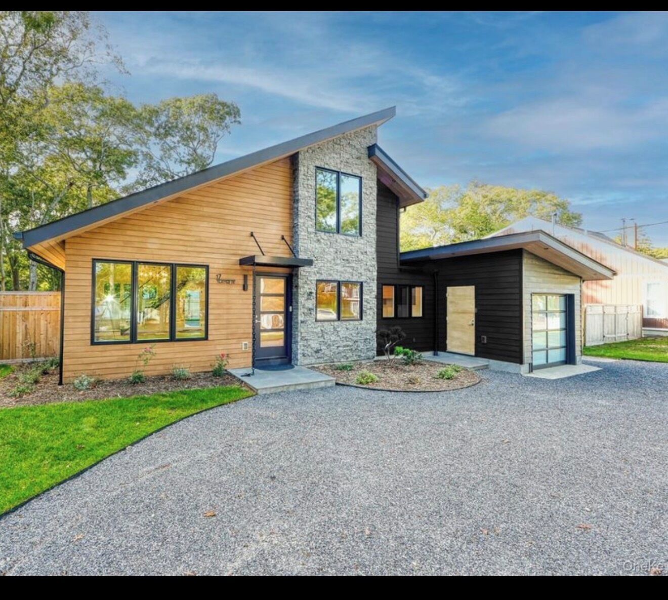 Et moderne hus i to etager med en stenvæg, store vinduer og en grusindkørsel.