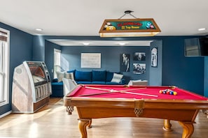 Ein Billardtisch in einem Raum mit einem Schild darüber, einer Couch und einer Jukebox.
