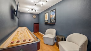 A room with a shuffleboard table, two chairs, a dartboard, and wall-mounted artwork. - Janis, Cozy 1-Bedroom Retreat in Gladheart, Sleeps 4, Hot Tub & Fire Pit (Fredericksburg)